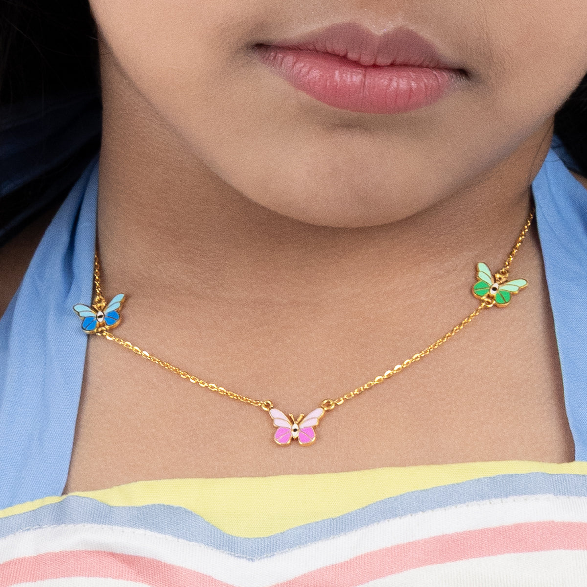 Tiny Jewels gold butterfly necklace worn by a person with a colorful striped shirt