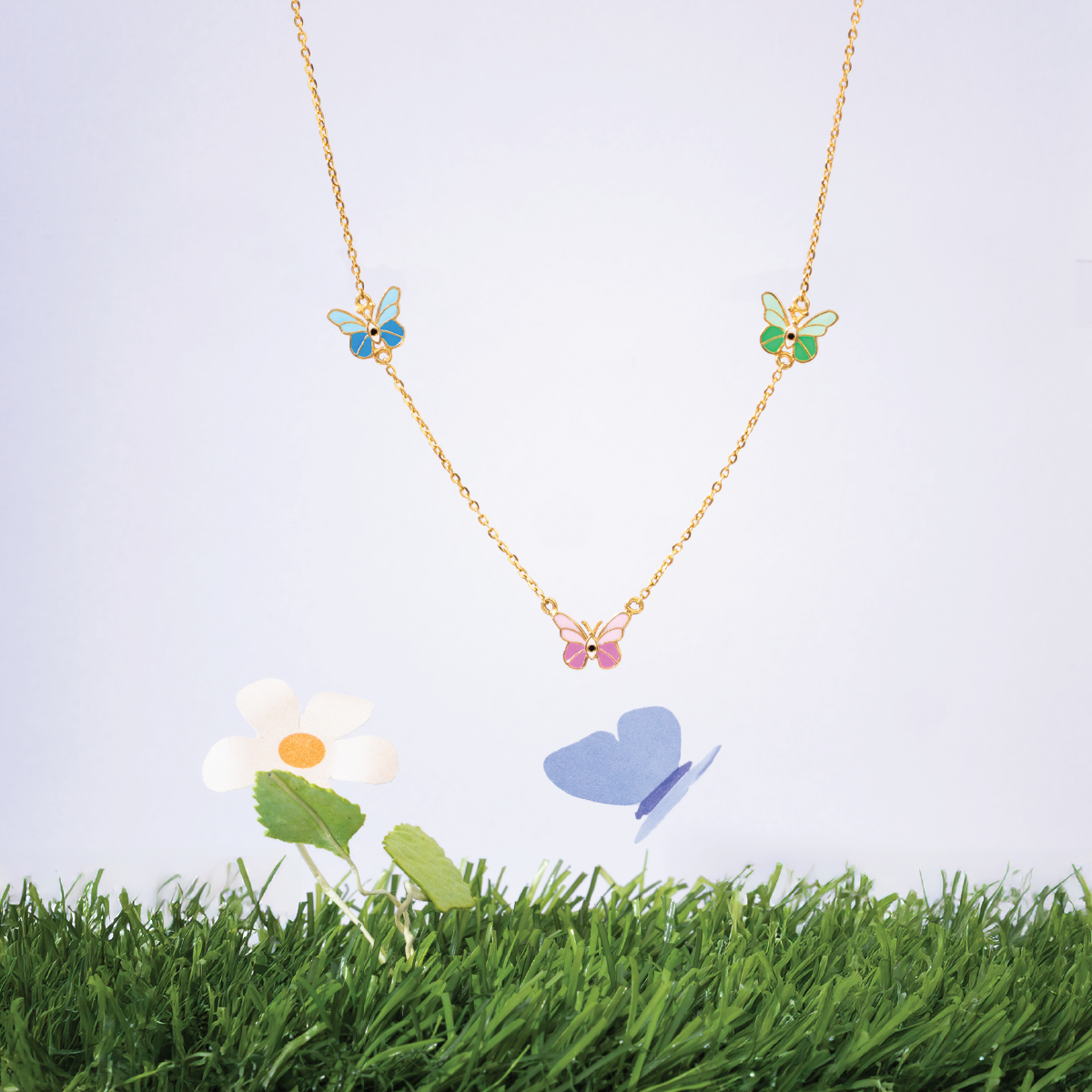 Tiny Jewels necklace with butterfly pendants on a grassy background