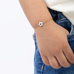 Tiny Jewels child's hand wearing a gold bracelet with a blue and white bead on a plain background