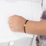 Tiny Jewels hand wearing a black beaded bracelet with a yellow flower charm on a white background