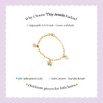Tiny Jewels gold bracelet with charms on a light purple background, featuring text about Tiny Jewels Kadas.
