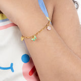 Tiny Jewels gold bracelet with charms on a child's wrist against a colorful background