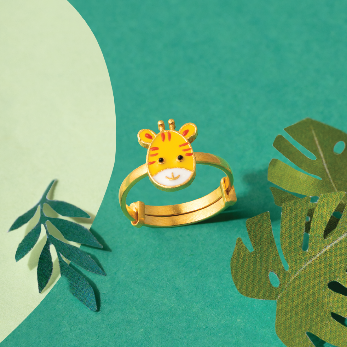 Tiny Jewels gold ring with tiger face design on a green background with leaves