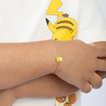 Tiny Jewels gold bracelet with a sun charm worn on a wrist, with a cartoon character in the background.