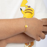 Tiny Jewels gold bracelet with a sun charm worn on a wrist, with a cartoon character in the background.