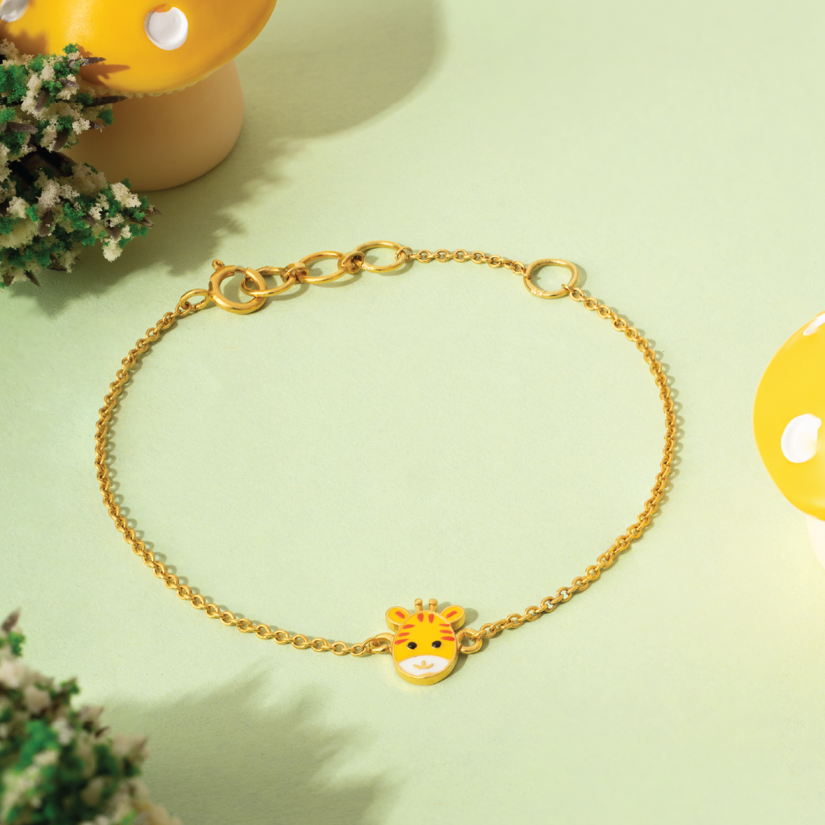 Tiny Jewels gold bracelet with a giraffe charm on a light green background