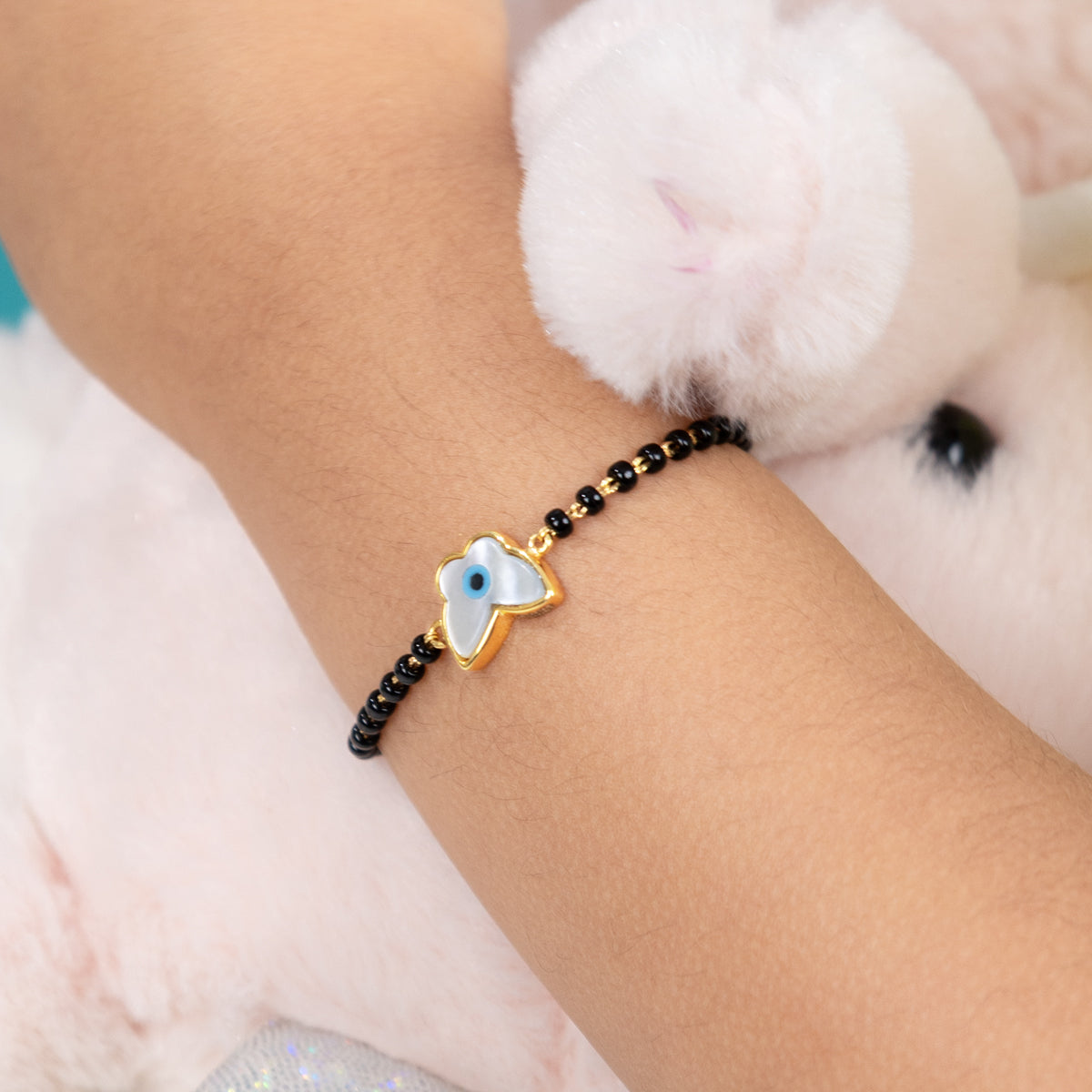 Tiny Jewels bracelet with a blue evil eye charm on a wrist, with a fluffy white toy in the background