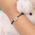 Tiny Jewels bracelet with a blue evil eye charm on a wrist, with a fluffy white toy in the background