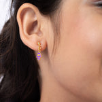 Tiny Jewels close-up of an ear wearing a gold earring with a purple hamsa design.