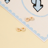 Tiny Jewels pair of gold and pink infinity symbol earrings on a decorative card with blue and black designs.