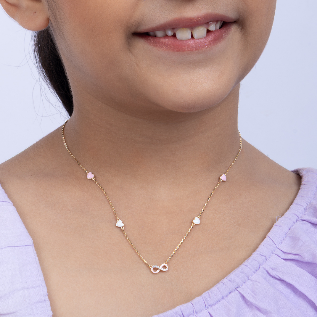 Tiny Jewels child wearing a gold necklace with heart-shaped pendants on a light background