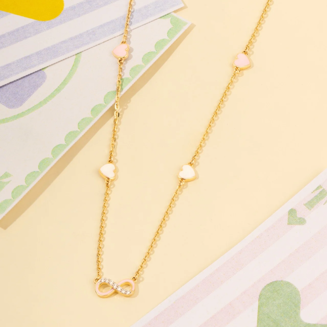 Tiny Jewels gold necklace with heart and infinity symbol charms on a colorful background