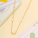 Tiny Jewels gold necklace with heart and infinity symbol charms on a colorful background