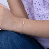 Tiny Jewels close-up of a wrist wearing a delicate bracelet with a pink flower charm, against a blurred background.