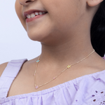 Tiny Jewels child wearing a delicate gold necklace with floral pendants against a light purple background
