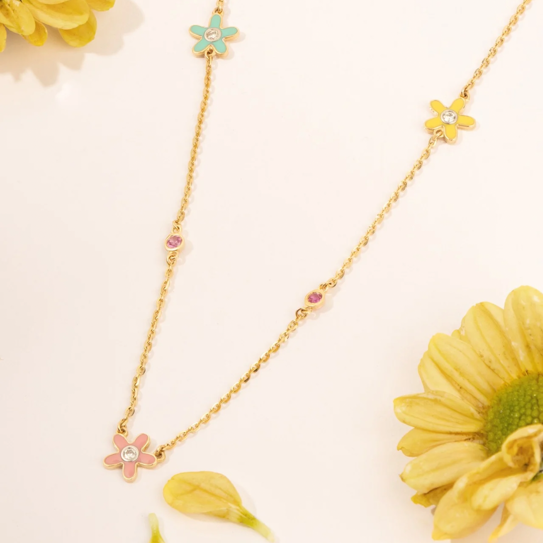 Tiny Jewels gold necklace with floral pendants on a light background with flowers