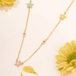 Tiny Jewels gold necklace with floral pendants on a light background with flowers