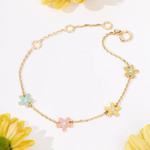 Tiny Jewels gold bracelet with colorful flower charms on a white background with flowers.