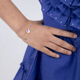 Tiny Jewels gold bracelet with purple accents on a wrist against a blue dress background