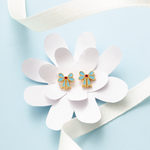Tiny Jewels gold and blue bow-shaped earrings on a white flower with a light blue background
