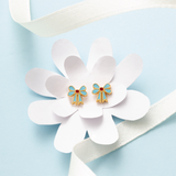 Tiny Jewels gold and blue bow-shaped earrings on a white flower with a light blue background