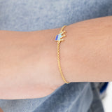 Tiny Jewels gold bracelet with a blue and white heart charm on a wrist against a denim background