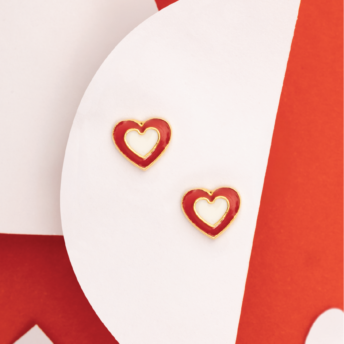 Tiny Jewels heart-shaped earrings with gold border on a red and white background