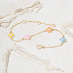 Tiny Jewels gold bracelet with colorful flower-shaped charms on a marble surface