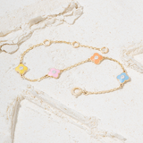 Tiny Jewels gold bracelet with colorful flower-shaped charms on a marble surface