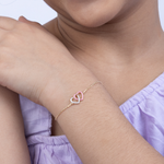 Tiny Jewels close-up of a person wearing a delicate bracelet with heart-shaped charms on a plain background