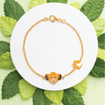 Tiny Jewels gold bracelet with a character charm on a white plate surrounded by green leaves