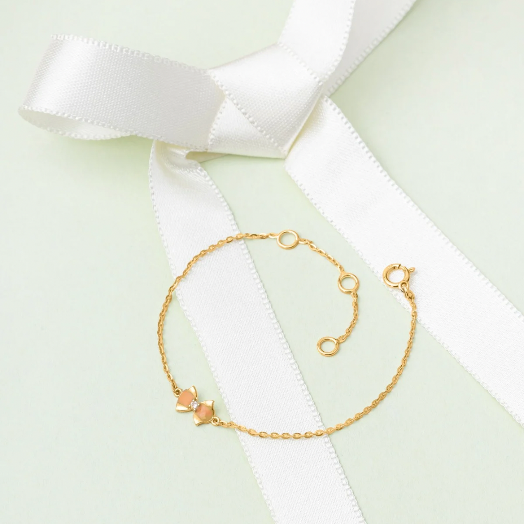 Tiny Jewels gold bracelet on a white ribbon with a light green background