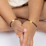 Tiny Jewels two hands holding each other wearing black beaded bracelets with gold accents.