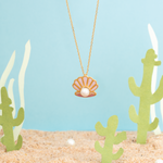 Tiny Jewels necklace with a shell pendant on a beach-themed background