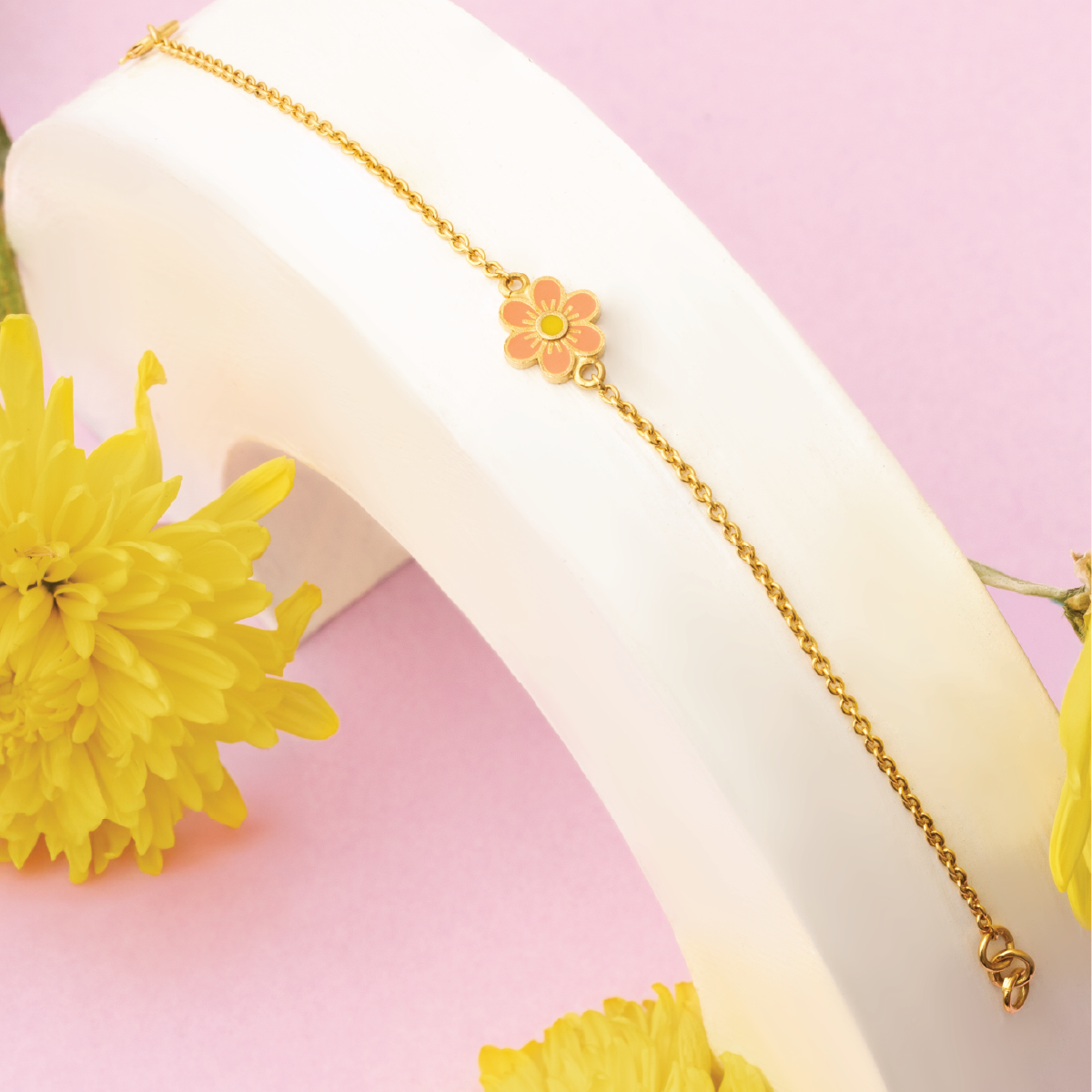Tiny Jewels gold anklet with floral charm on a white surface with yellow flowers