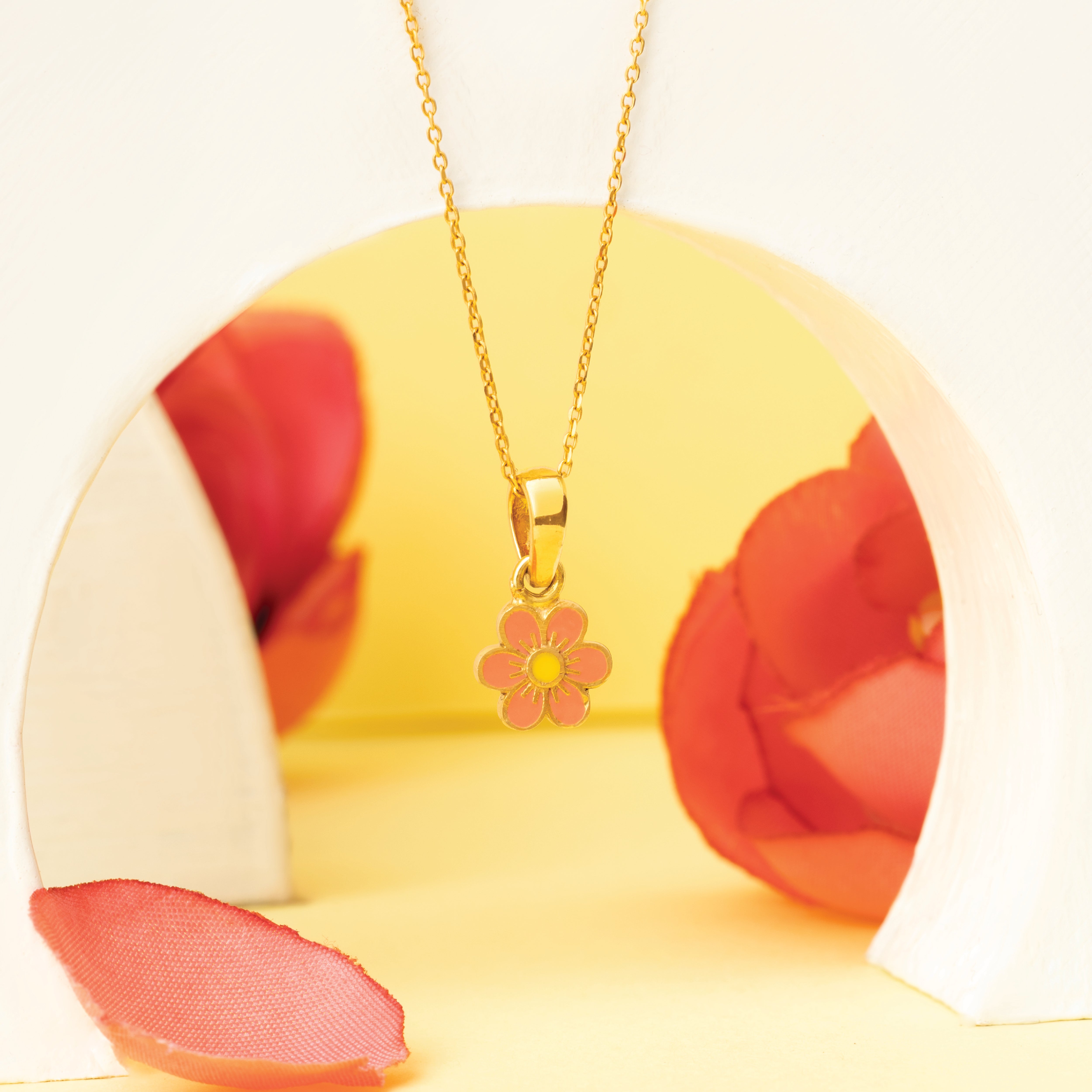Tiny Jewels gold necklace with a pink flower pendant on a yellow and red floral background