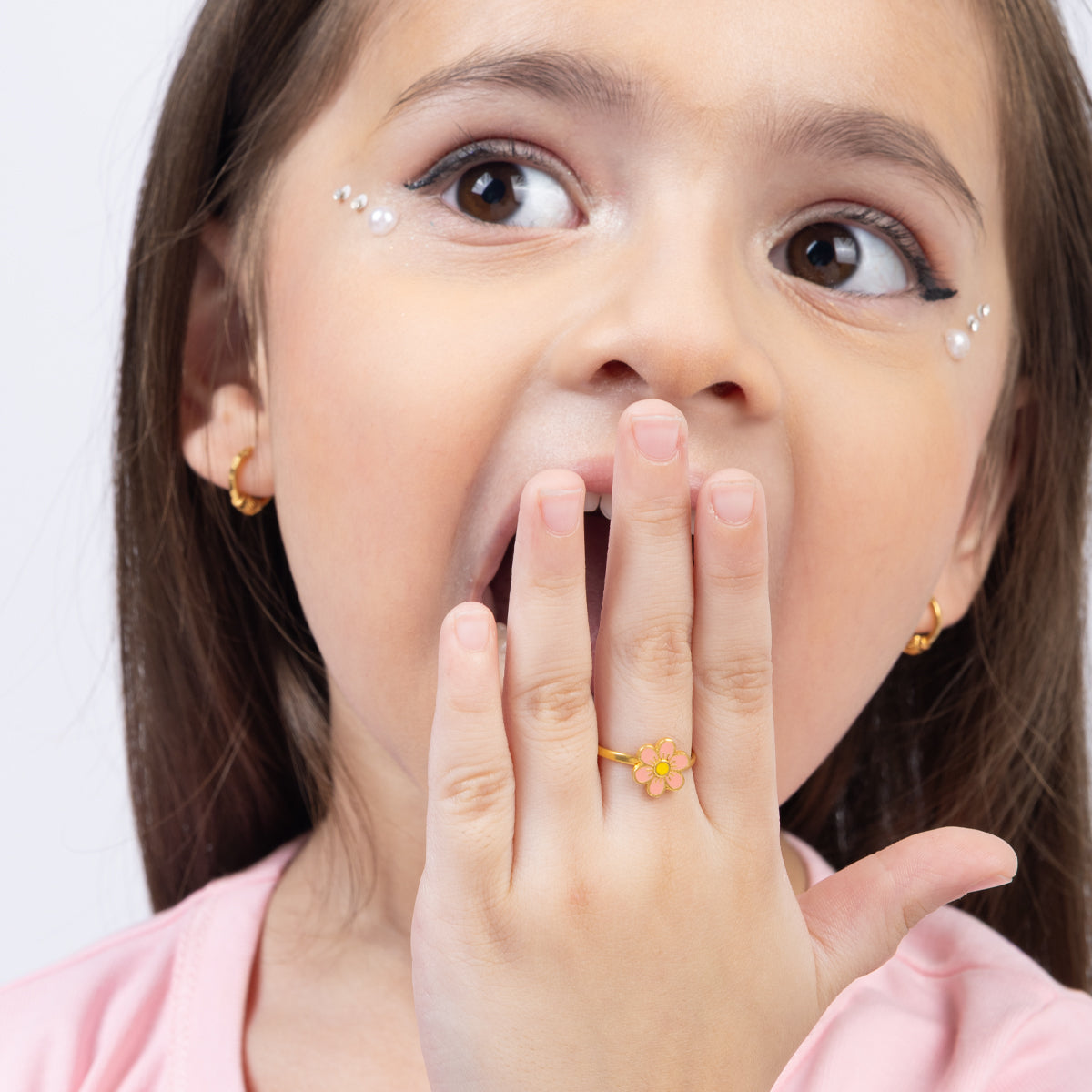 Tiny Jewels young girl with a surprised expression, covering her mouth with her hand.