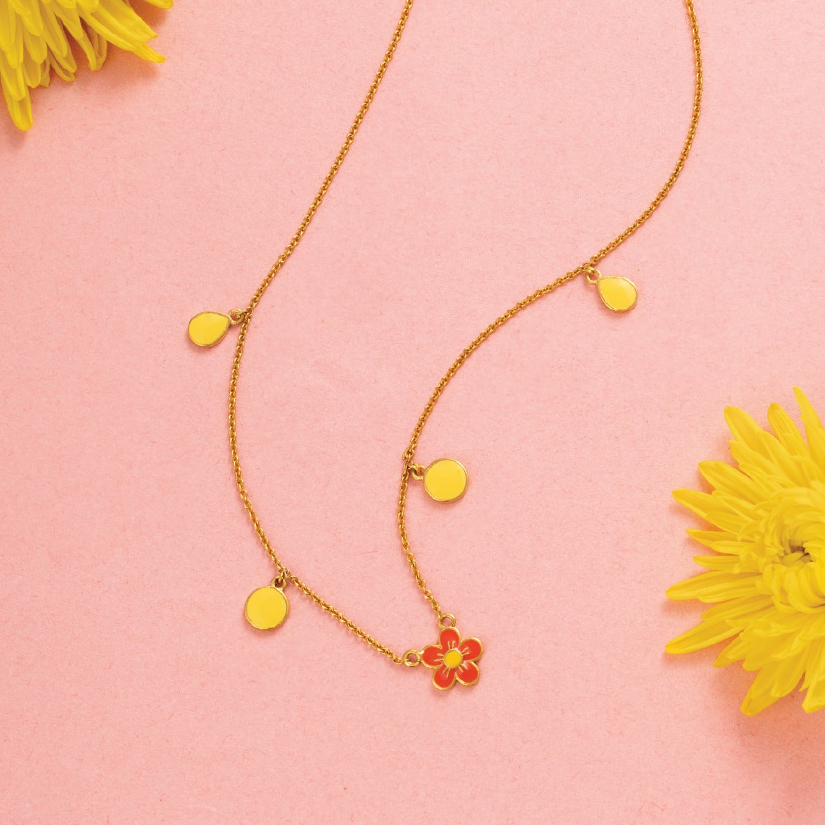 Tiny Jewels necklace with yellow pendants on a pink background with yellow flowers