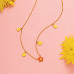 Tiny Jewels necklace with yellow pendants on a pink background with yellow flowers