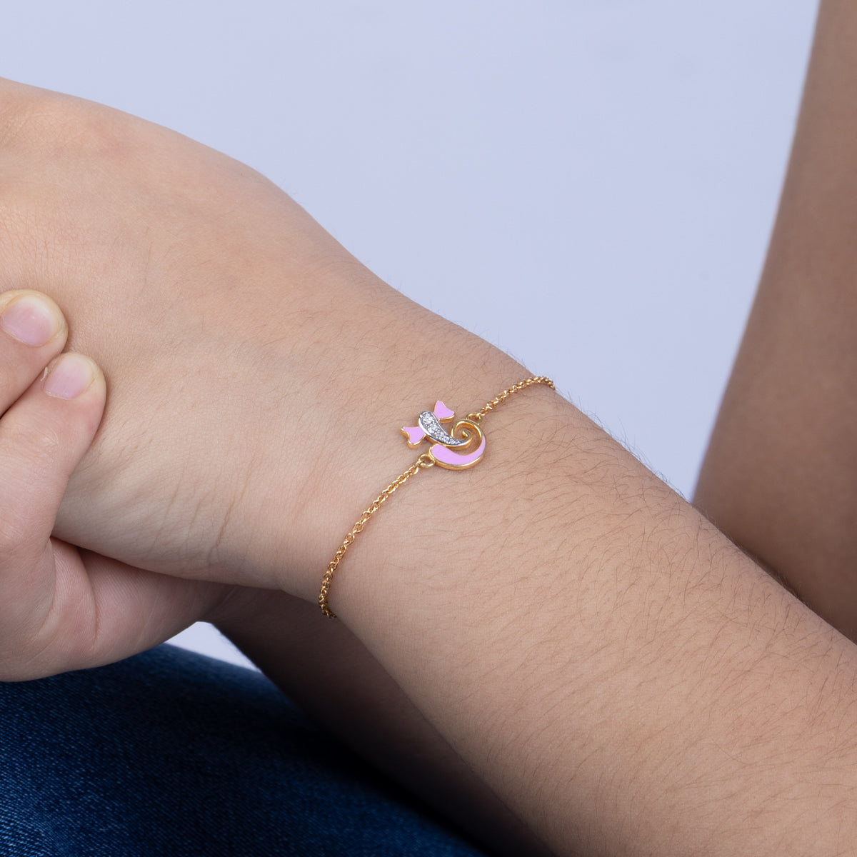 Tiny Jewels gold bracelet with a pink heart and star charm on a wrist against a light purple background