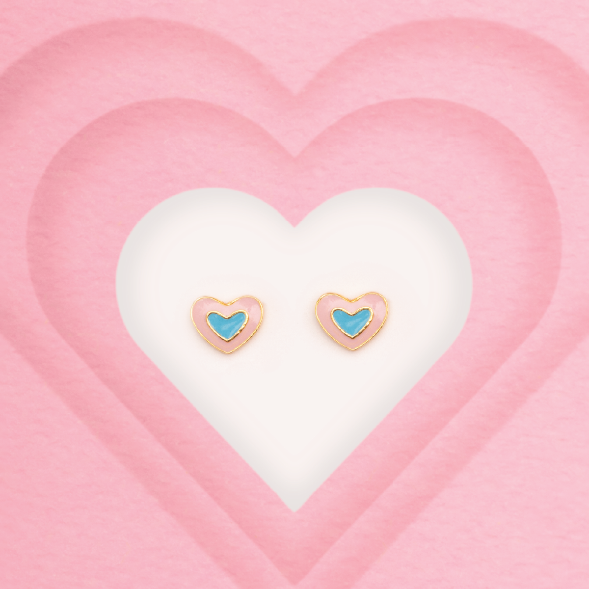 Tiny Jewels heart-shaped earrings with blue centers on a pink heart background