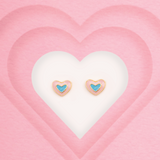 Tiny Jewels heart-shaped earrings with blue centers on a pink heart background