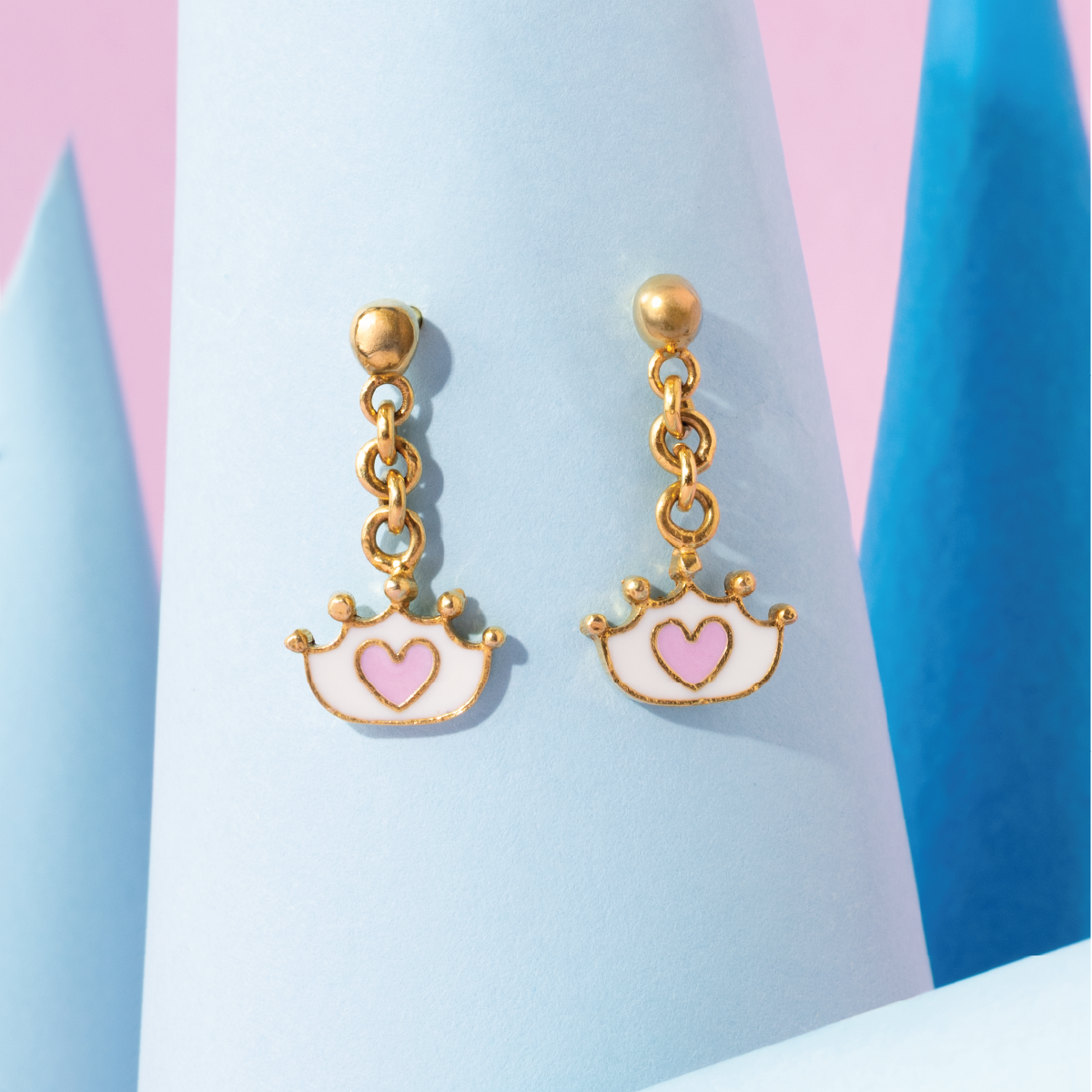 Tiny Jewels gold earrings with heart designs on a pastel background
