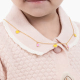 Tiny Jewels child wearing a gold necklace with colorful heart-shaped pendants on a pink outfit.