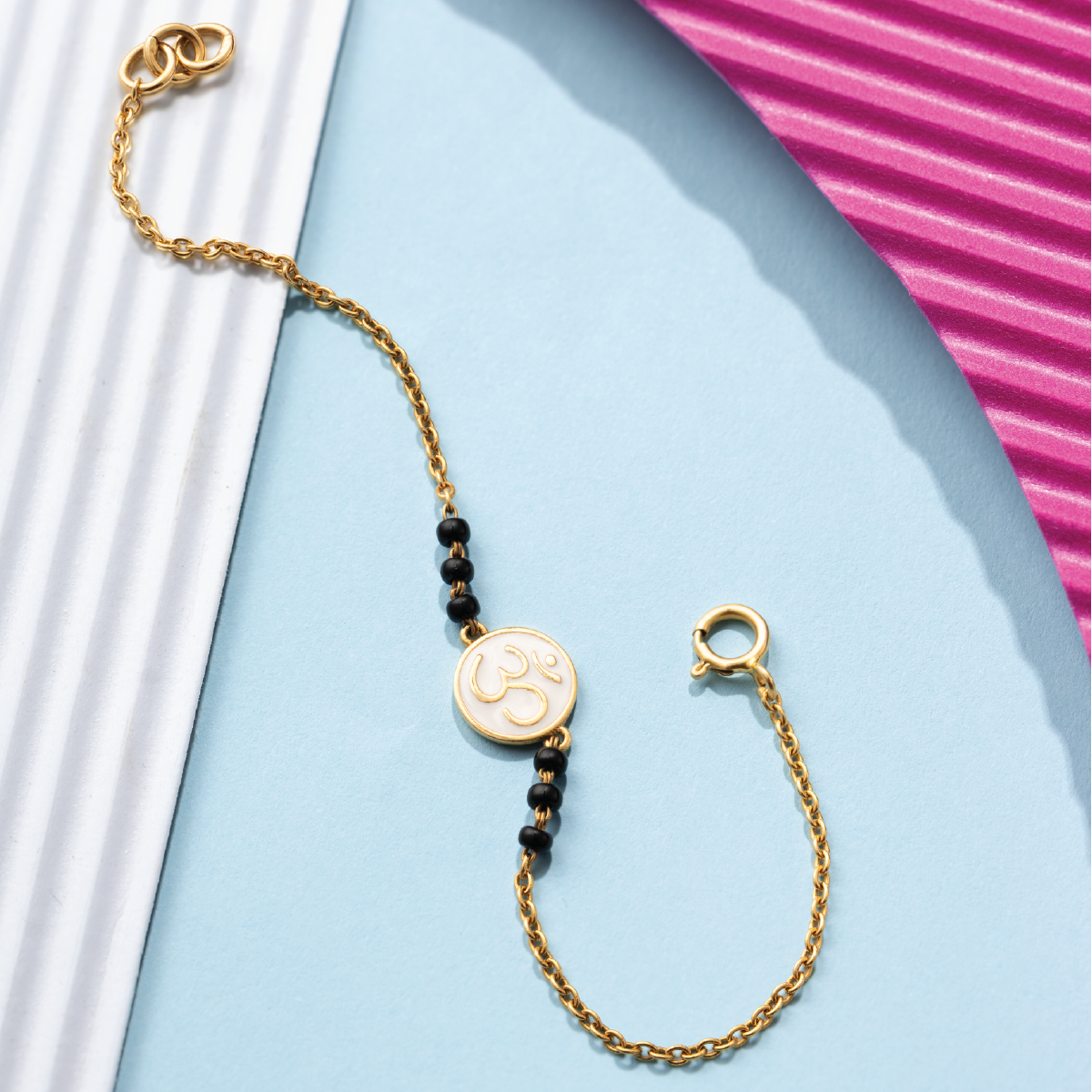 Tiny Jewels gold bracelet with black beads on a light blue background