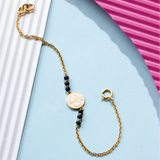 Tiny Jewels gold bracelet with black beads on a light blue background