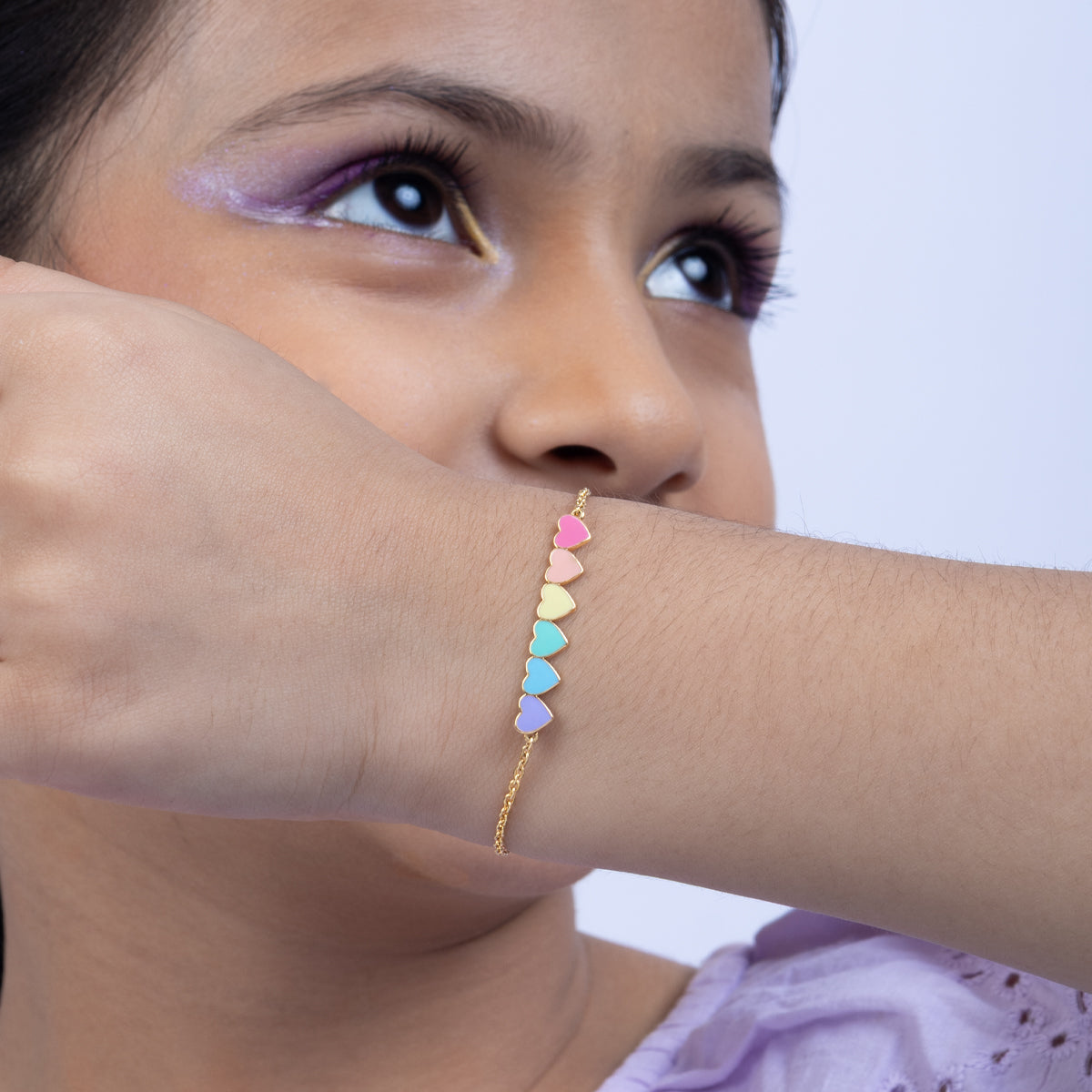 Tiny Jewels close-up of a person wearing a colorful heart-shaped bracelet on a plain background