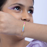 Tiny Jewels close-up of a person wearing a colorful heart-shaped bracelet on a plain background