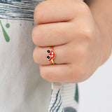 Tiny Jewels close-up of a hand wearing a small ring with a red and black design.