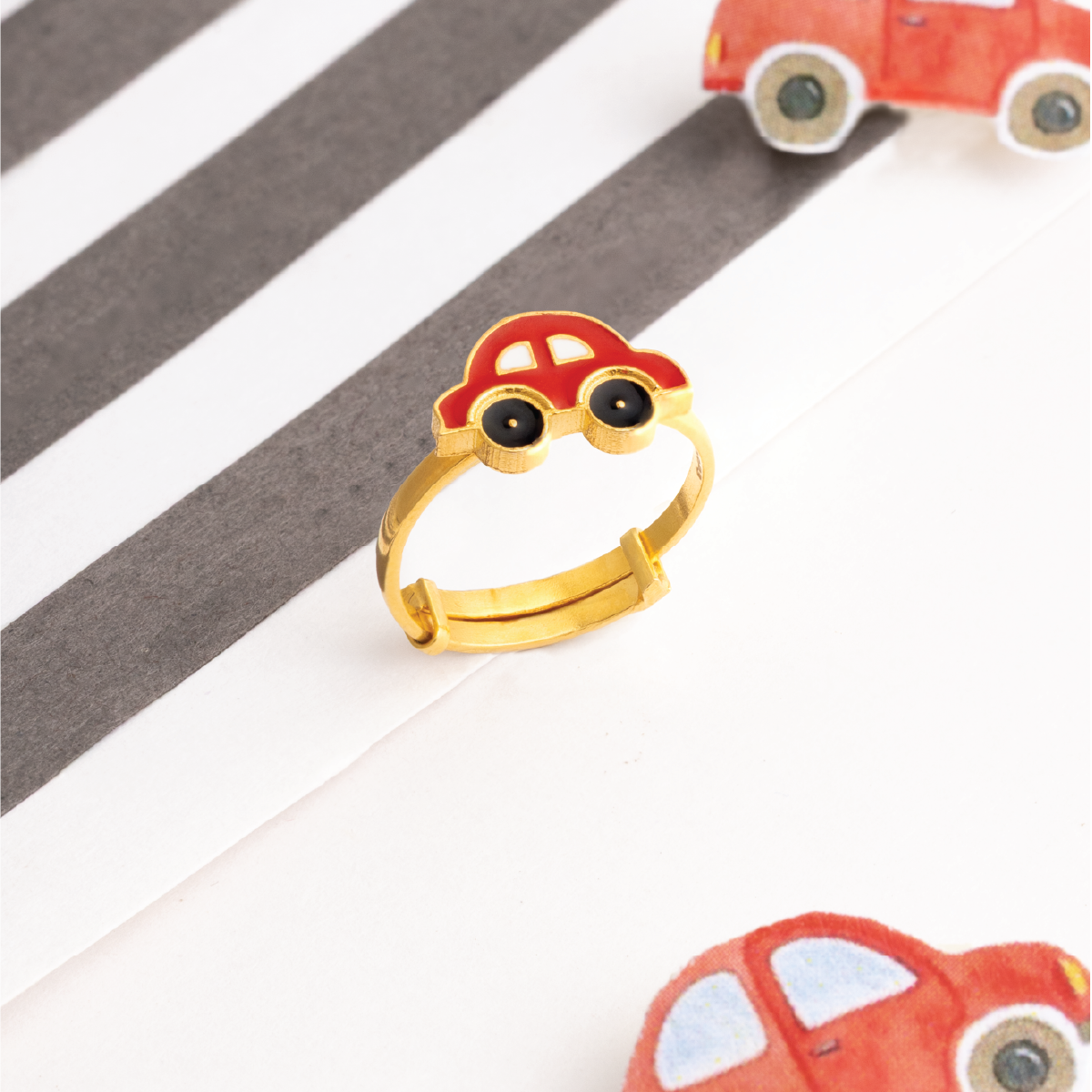 Tiny Jewels gold ring shaped like a car on a striped background with toy cars.